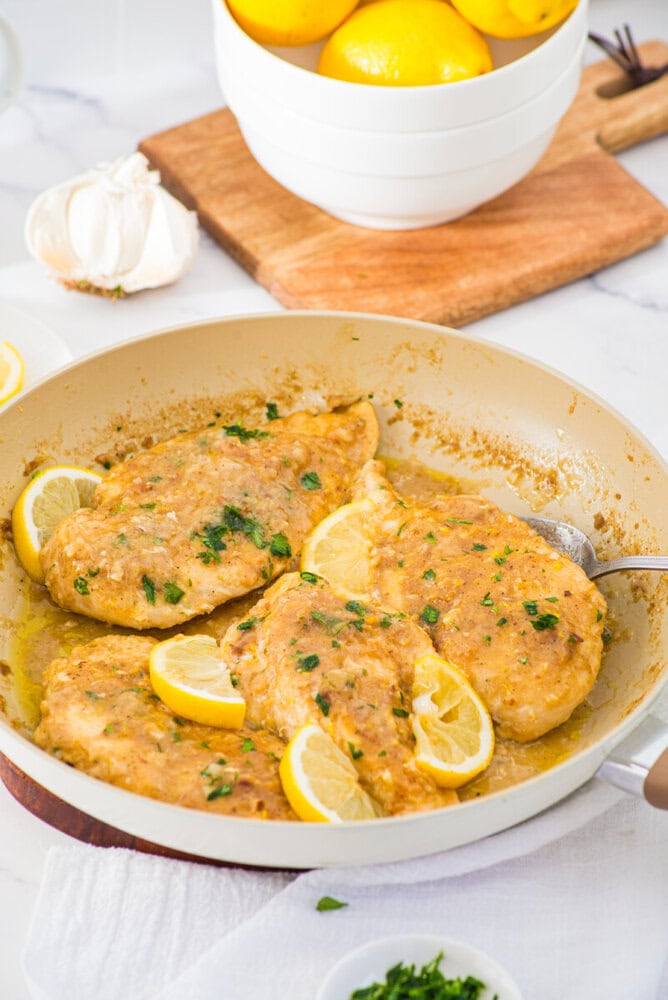 Lemon garlic chicken breasts in pan with lemon slices and parsley garnish