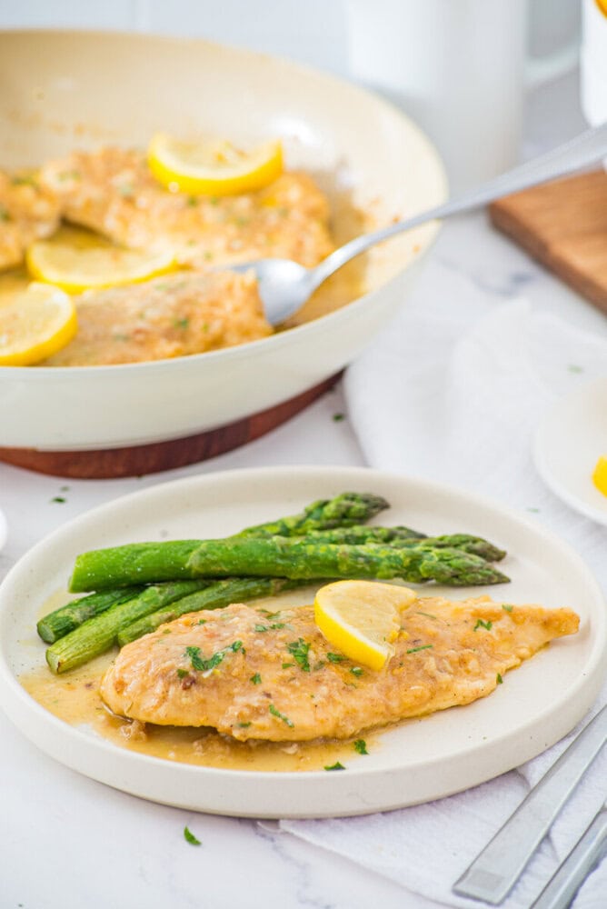 Plated lemon garlic chicken breast with asparagus and lemon garnish, ready to serve