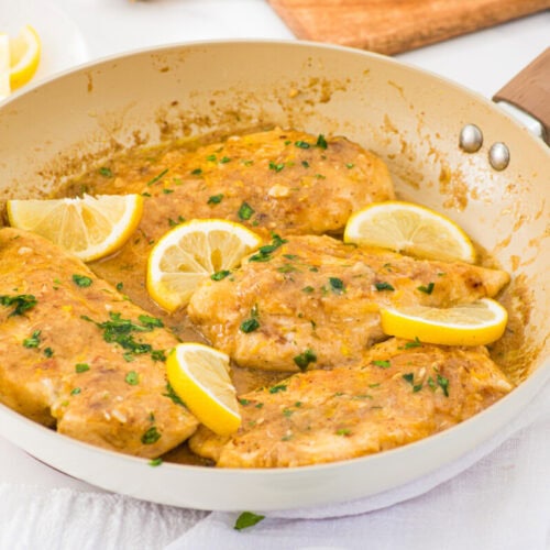 Lemon garlic chicken breasts in creamy sauce garnished with parsley and lemon slices in ceramic pan