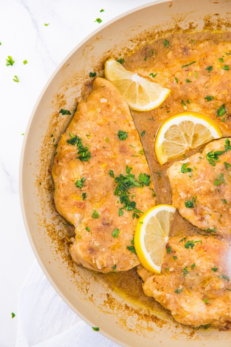 Lemon garlic chicken breast in skillet with fresh parsley and lemon garnish