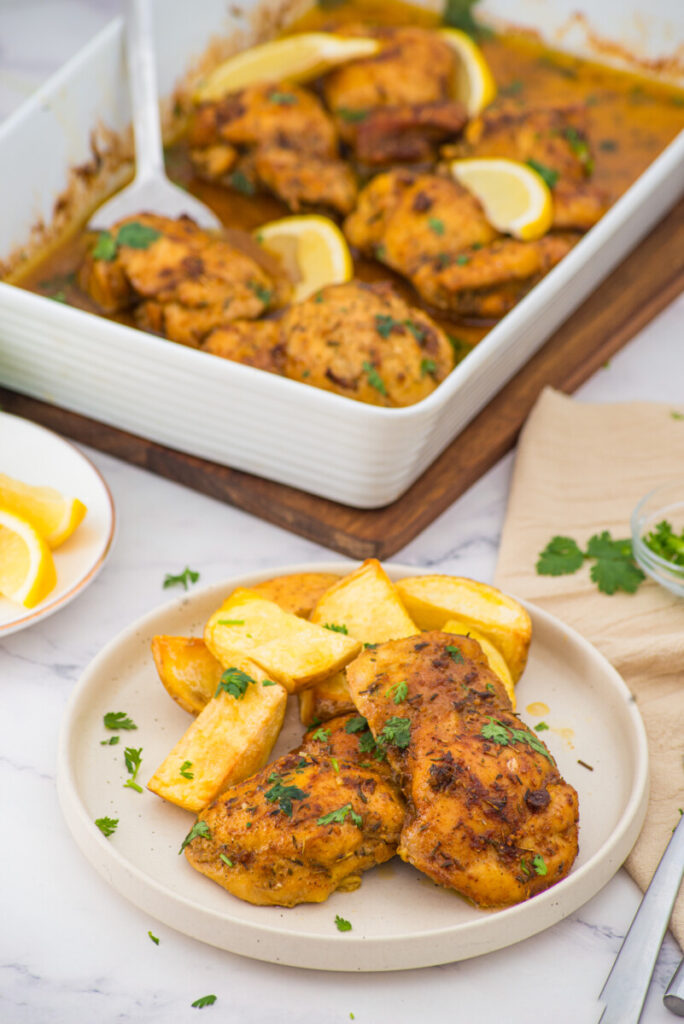 Oven baked boneless skinless chicken thighs with roasted potatoes and lemon garnish served on white plate