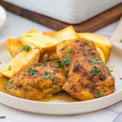 Oven baked boneless skinless chicken thighs with roasted potatoes and parsley garnish on a white plate