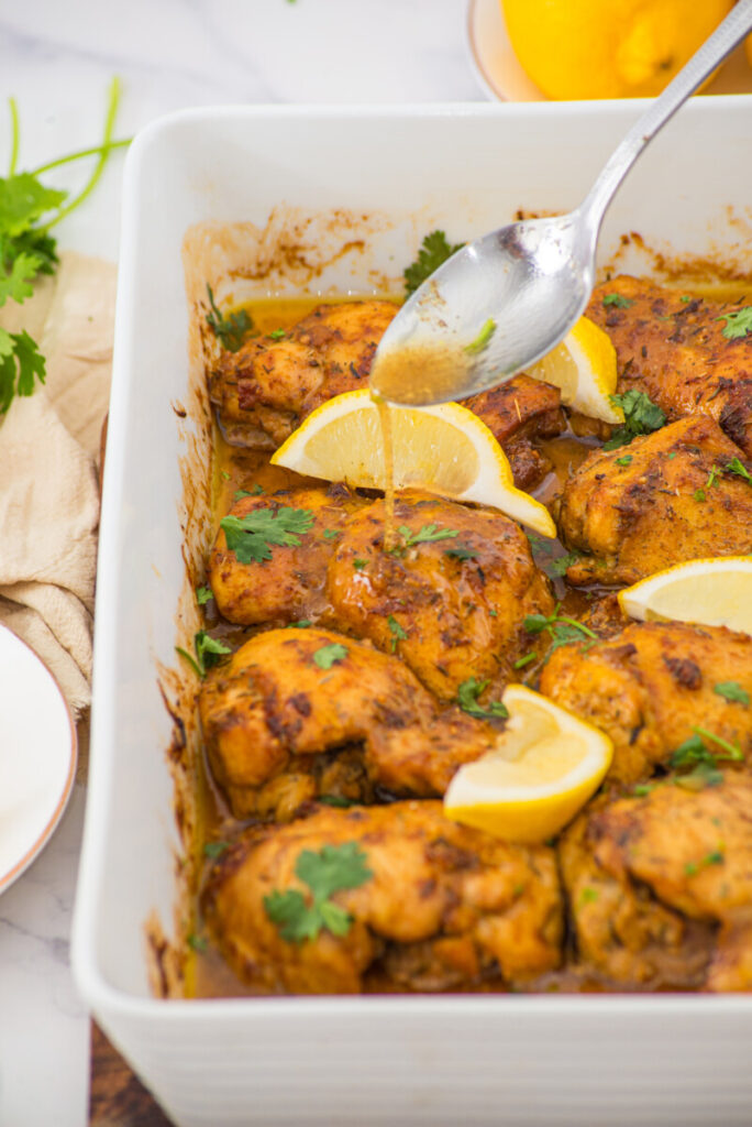 Oven baked boneless skinless chicken thighs in white dish garnished with lemon and cilantro
