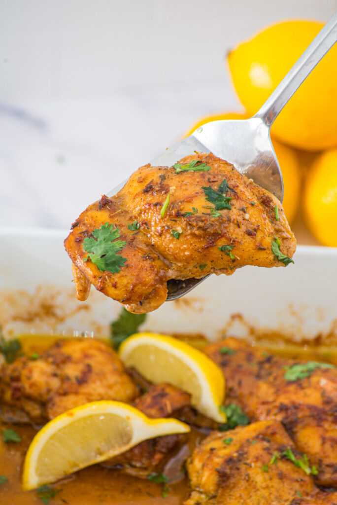 Oven baked boneless skinless chicken thigh on spoon with lemon garnish and fresh cilantro