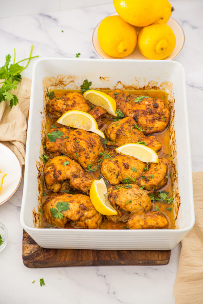 Oven baked boneless skinless chicken thighs with lemon and parsley garnish in white baking dish