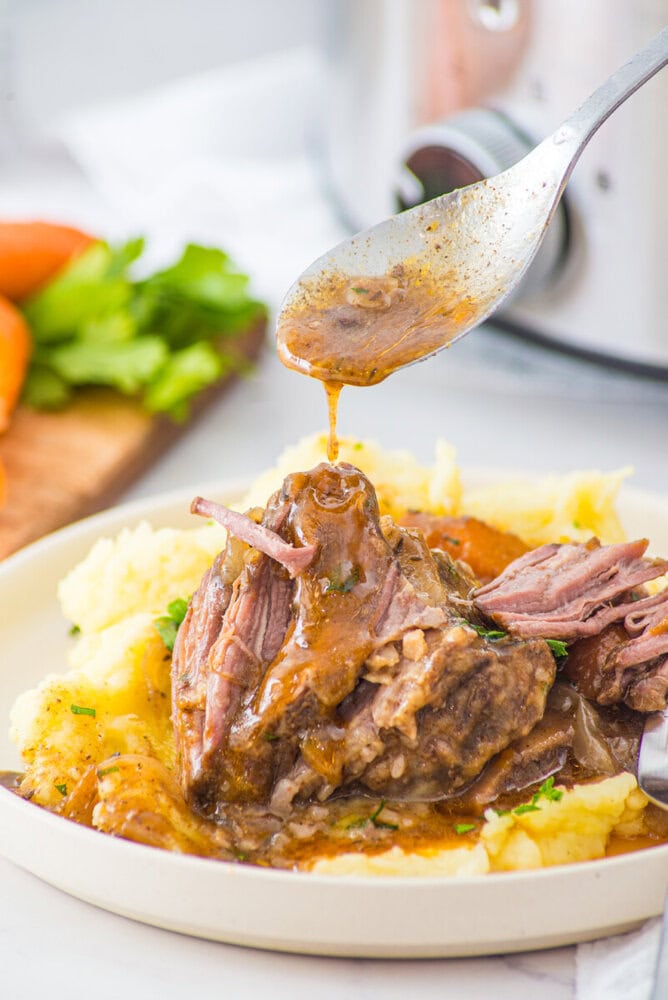 Slow cooker braised short ribs with mashed potatoes and gravy being drizzled from a spoon