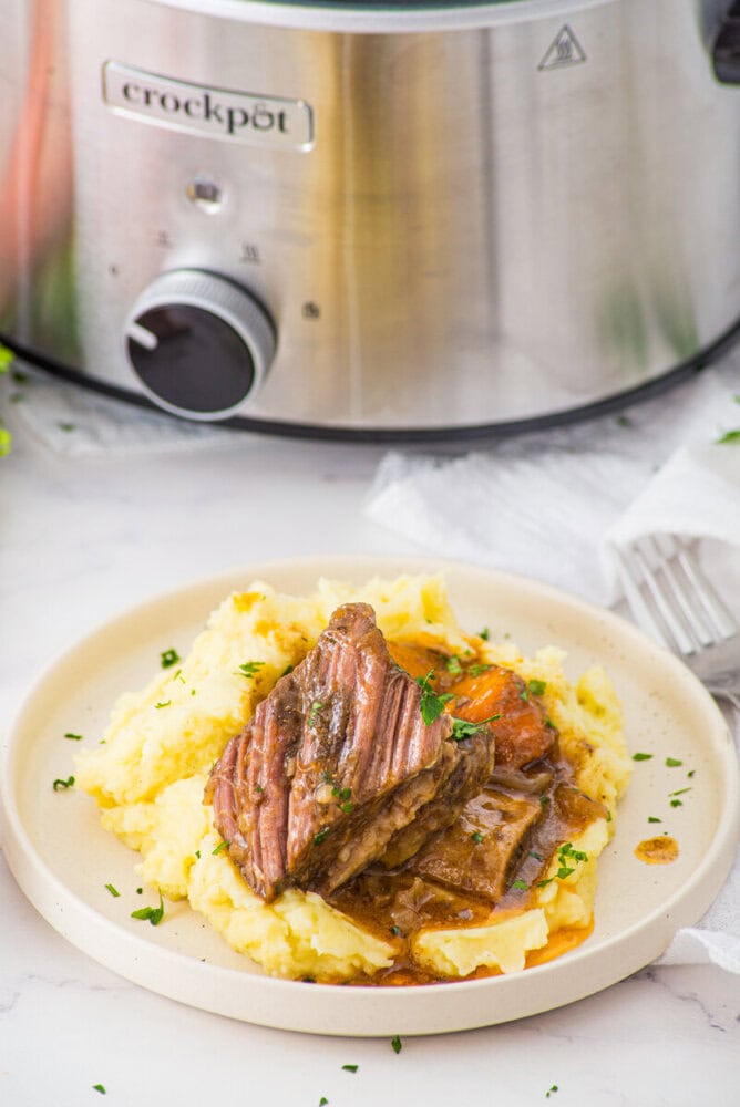 Slow cooker braised short ribs plated with mashed potatoes and gravy garnished with parsley