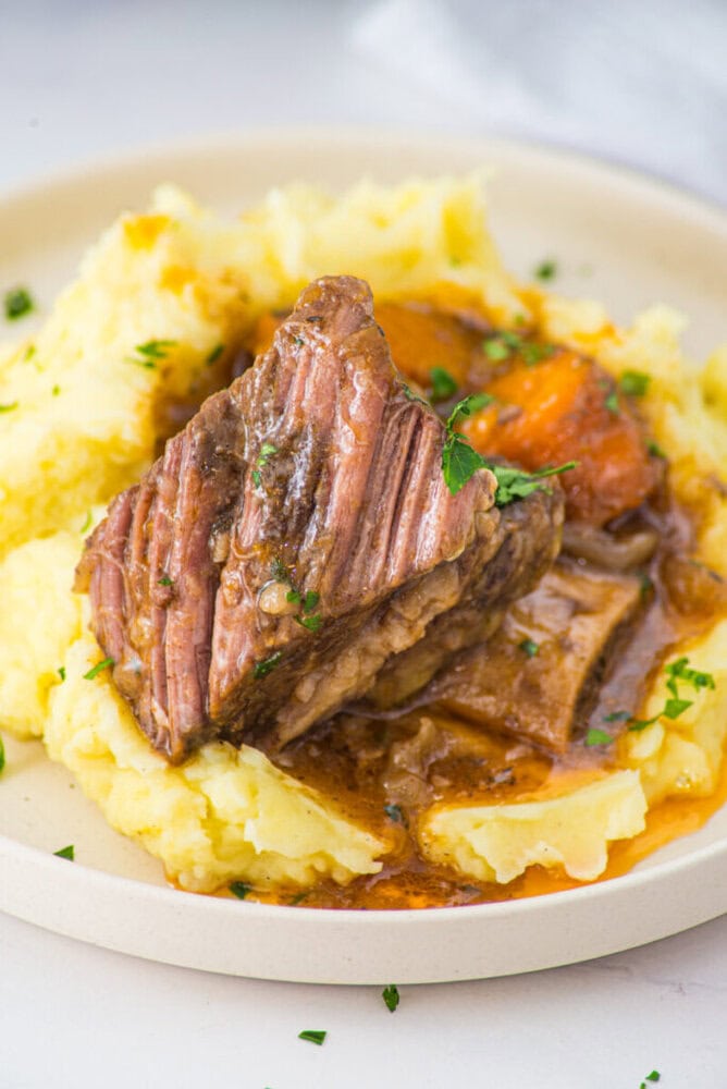 Slow cooker braised short ribs with mashed potatoes and parsley garnish on white plate