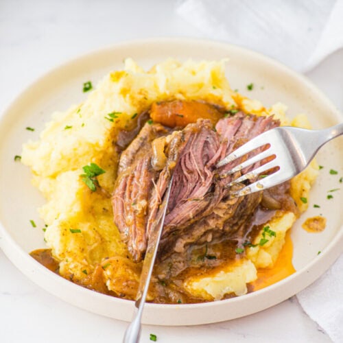 Slow cooker braised short ribs plated with mashed potatoes and gravy, fork lifting tender meat
