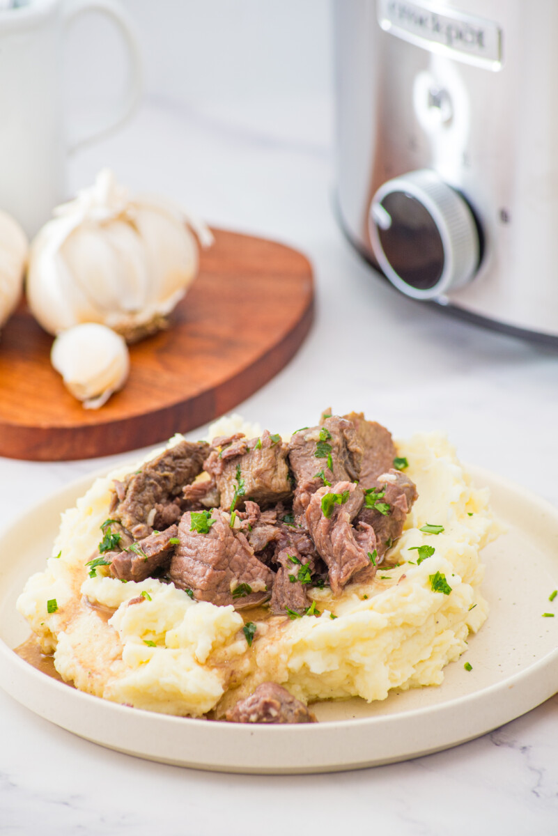 Slow cooker garlic butter steak bites served over mashed potatoes with chives garnish