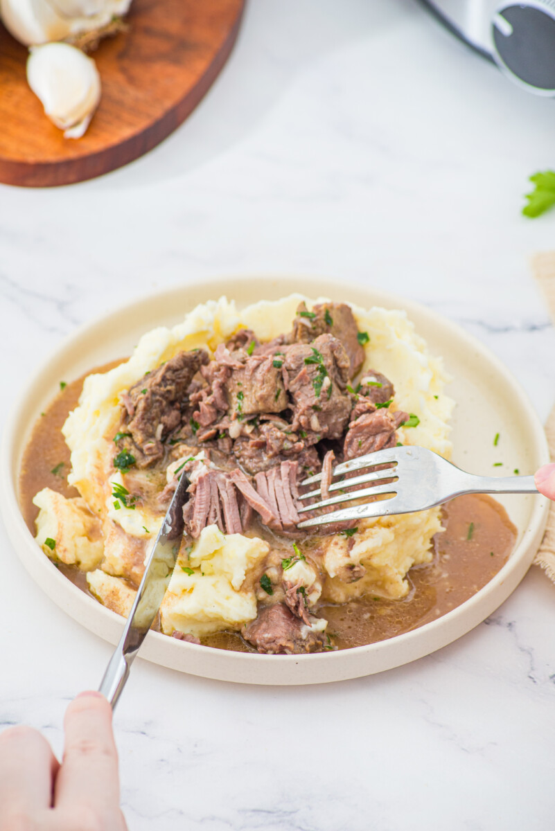 Slow cooker garlic butter steak bites with shredded beef and mashed potatoes on a white plate