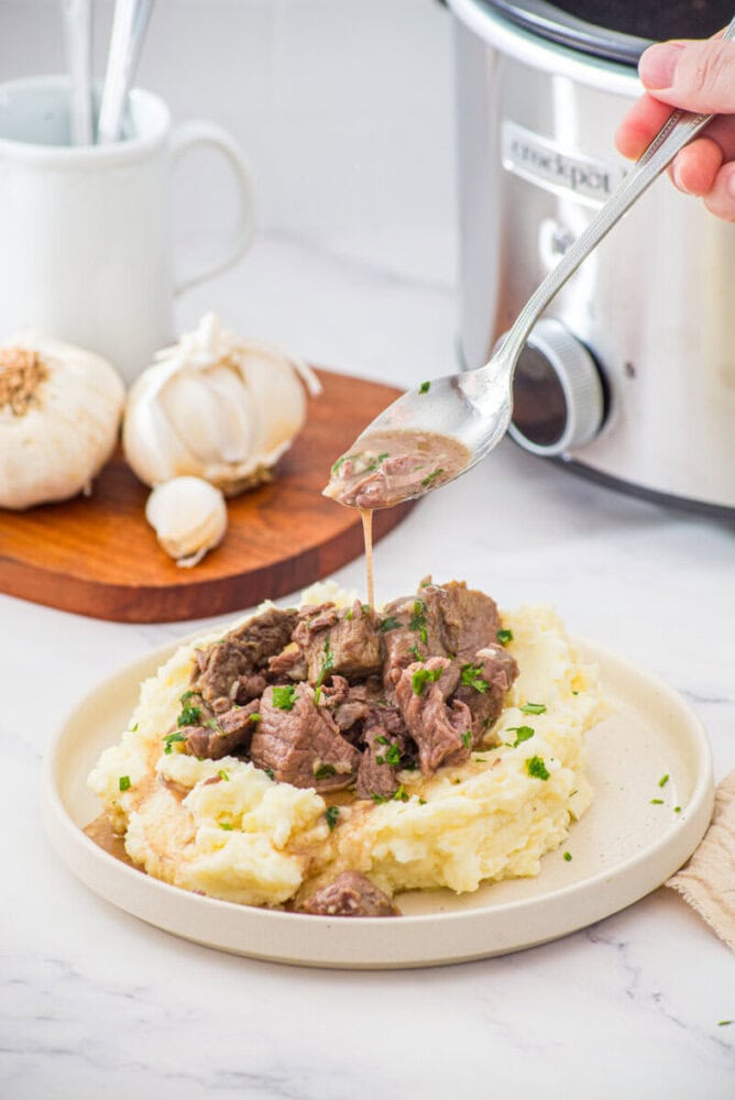 Slow cooker garlic butter steak bites served over creamy mashed potatoes with fresh parsley garnish