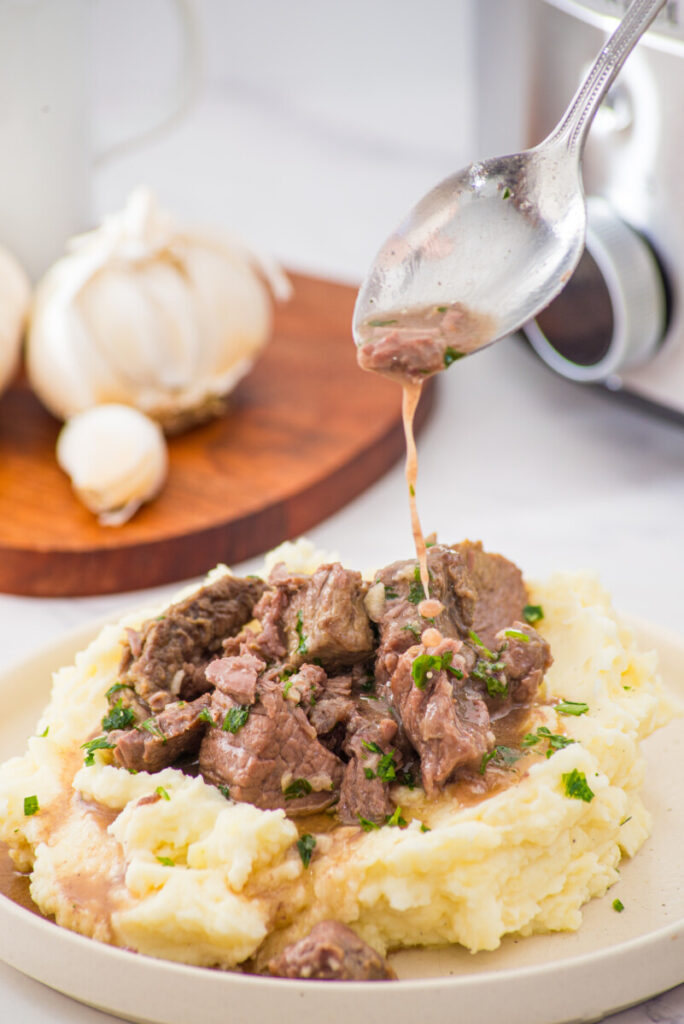 Slow cooker garlic butter steak bites served over mashed potatoes with fresh parsley and dripping sauce