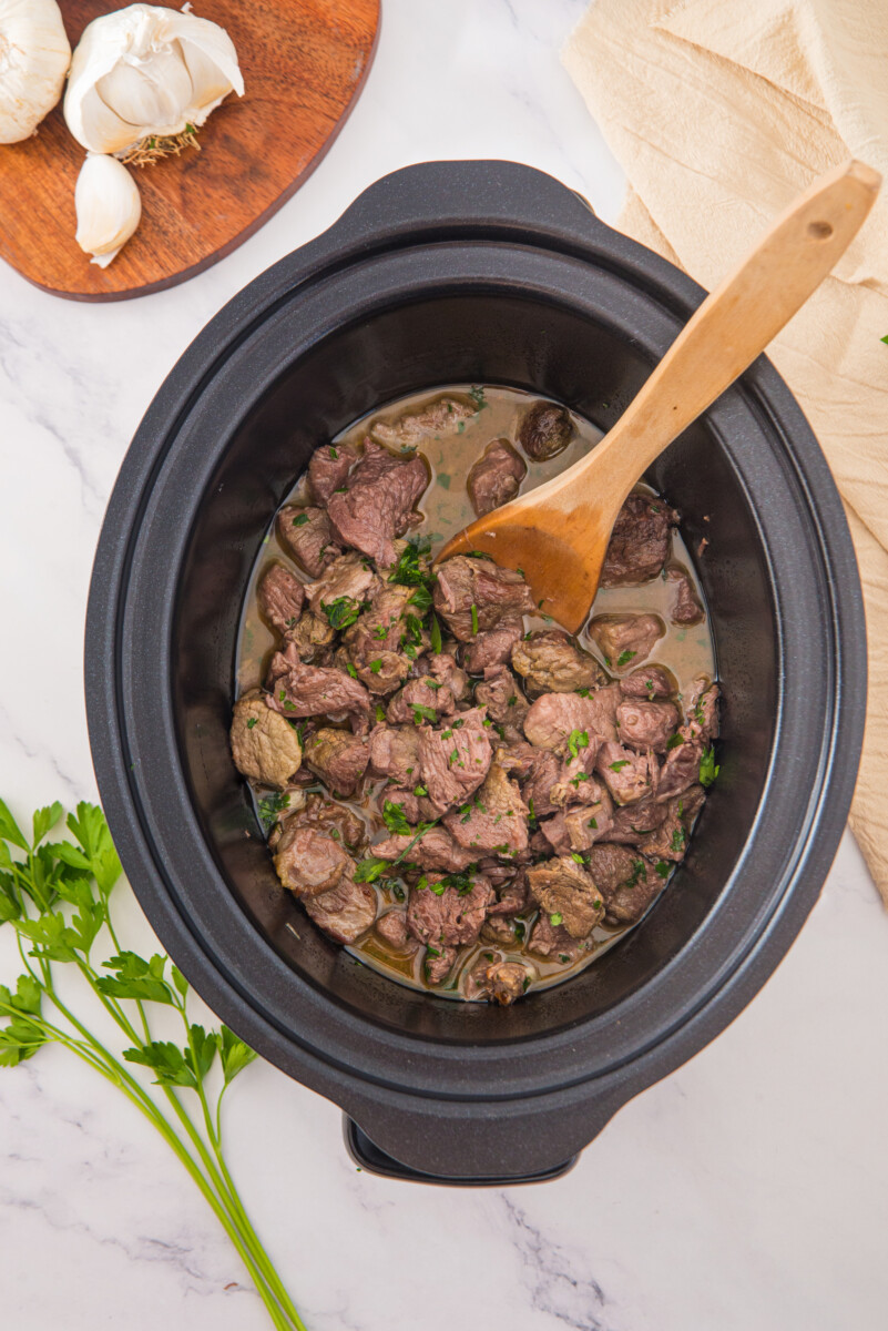 Slow cooker garlic butter steak bites in creamy sauce garnished with parsley
