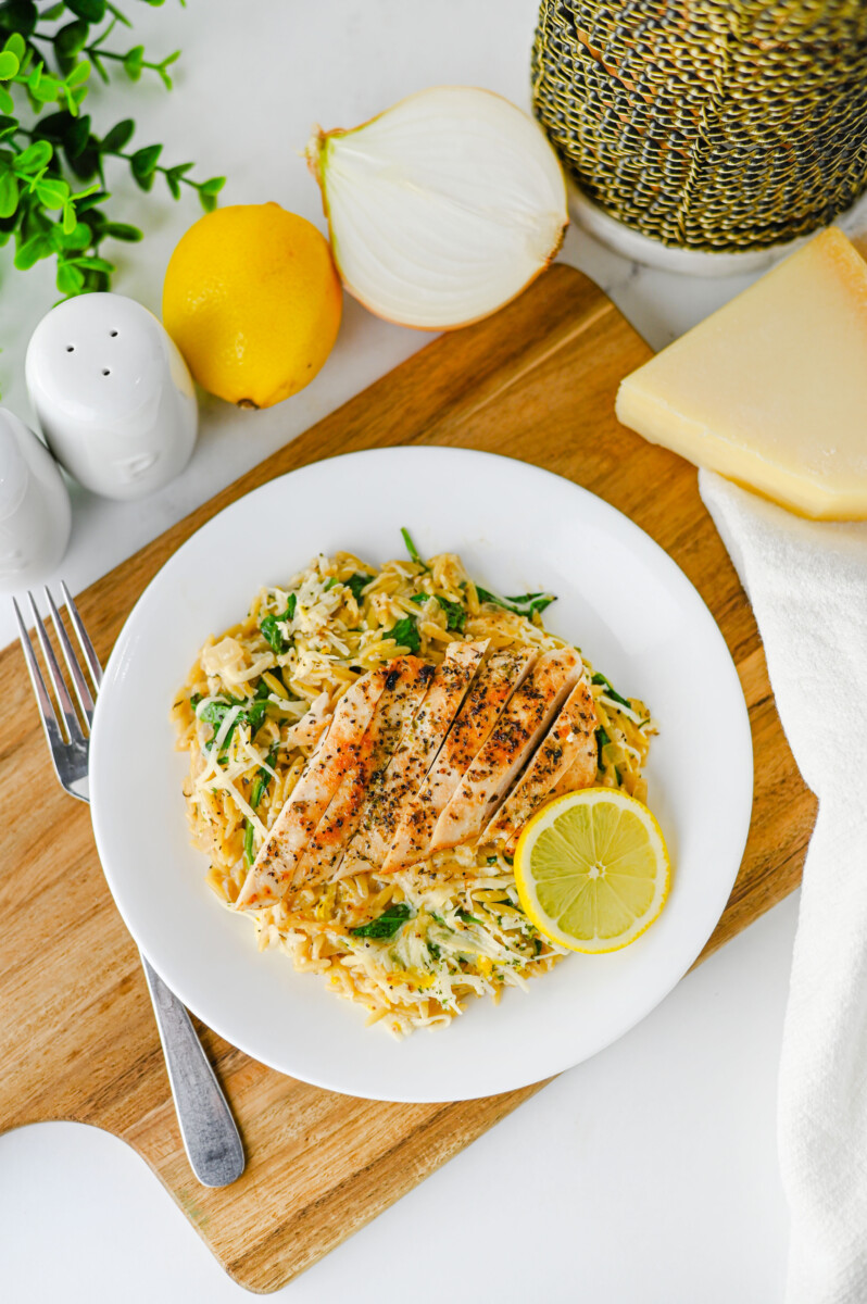 Creamy Lemon Parmesan Chicken Orzo with sliced chicken breast and lemon slice on white plate