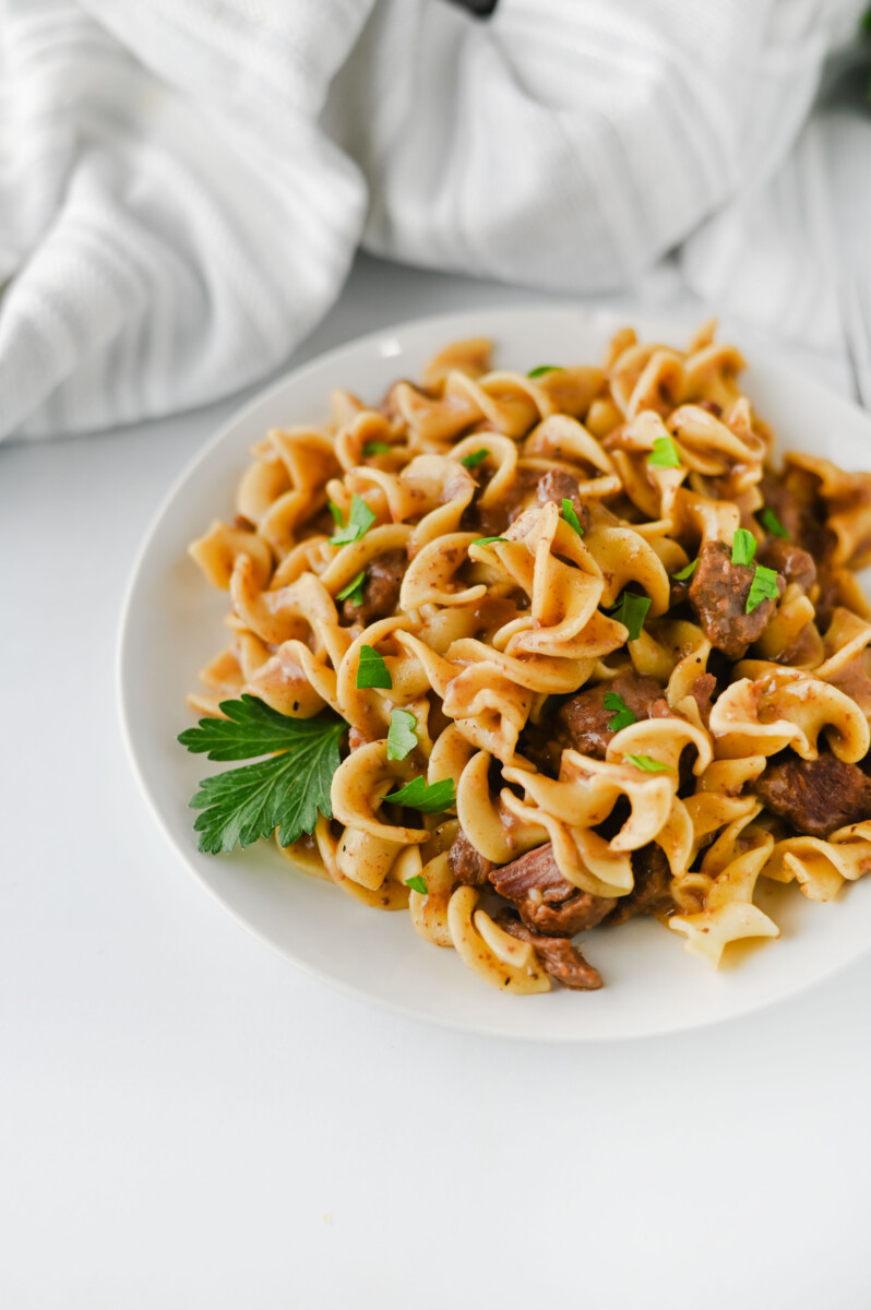 Crockpot beef and noodles stroganoff with parsley garnish on white plate