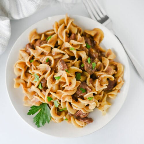 Crockpot beef and egg noodles garnished with parsley, plated and ready to serve
