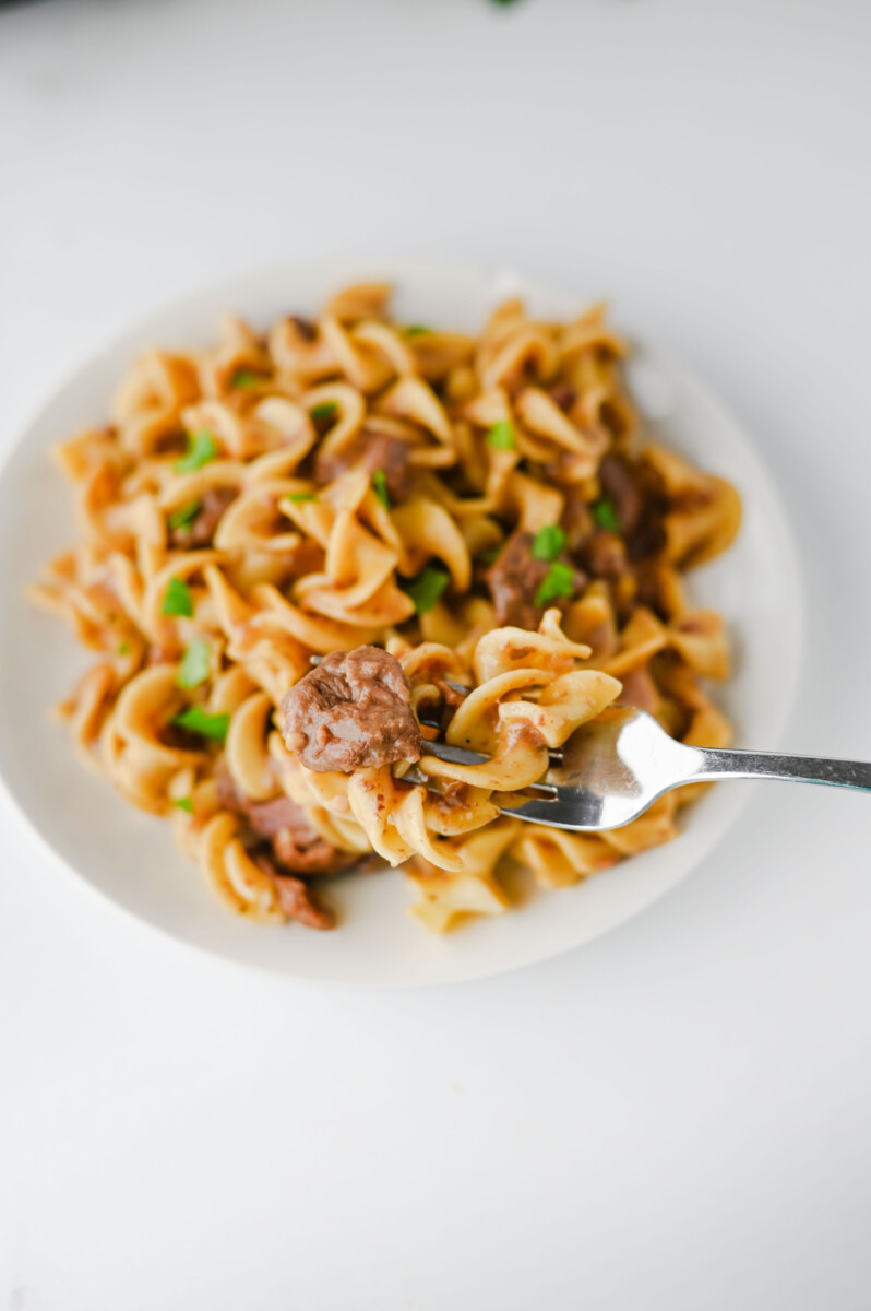 Crockpot beef and noodles plated on white dish with fork and green onion garnish