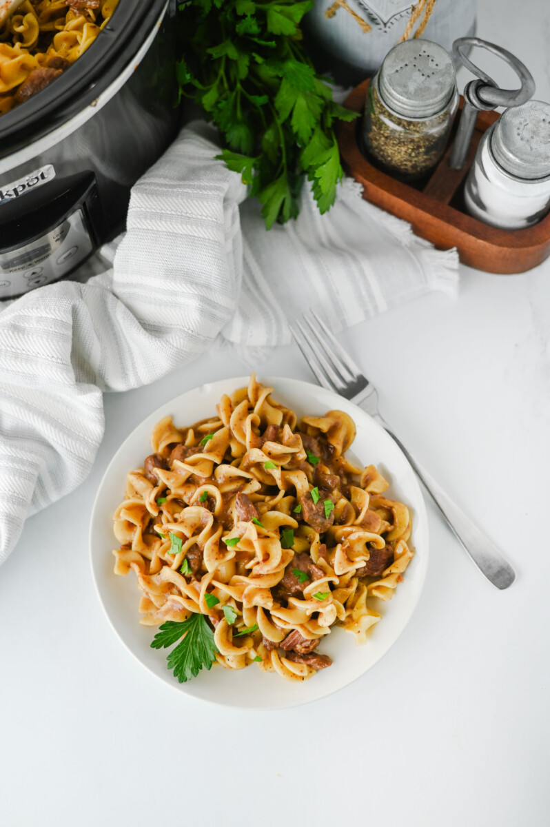 Crockpot beef and noodles plated on white dish with parsley garnish and fork