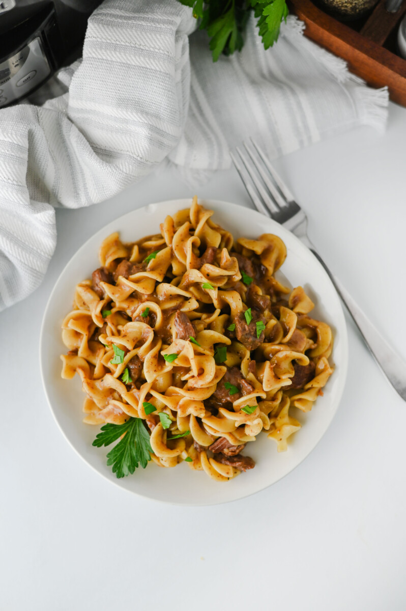 Crockpot beef and noodles served on white plate with parsley garnish and fork