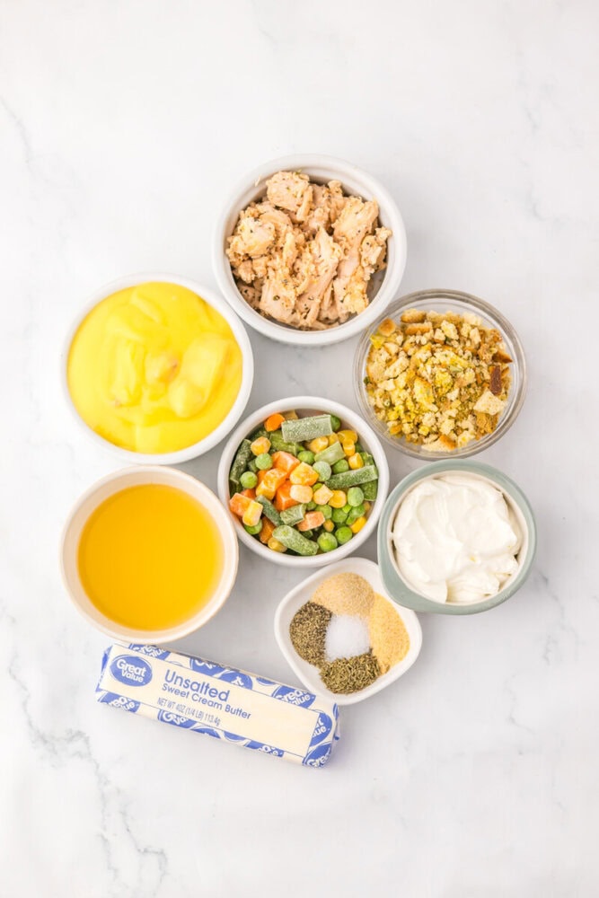 Chicken pot pie casserole ingredients arranged in bowls including cooked chicken, mixed vegetables, butter, cream, and seasonings