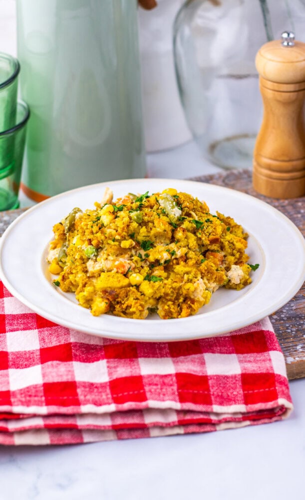 Chicken and corn casserole with herbs on white plate, red checkered napkin, ready to serve