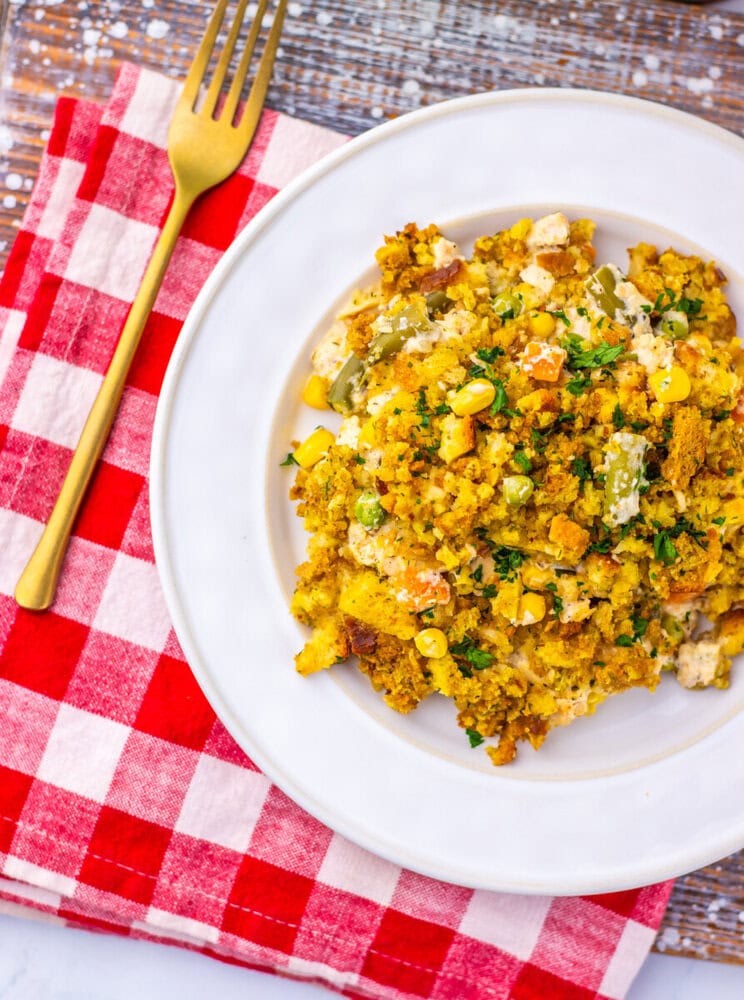 Chicken and stuffing pot pie casserole with corn and herbs on white plate with red checkered napkin