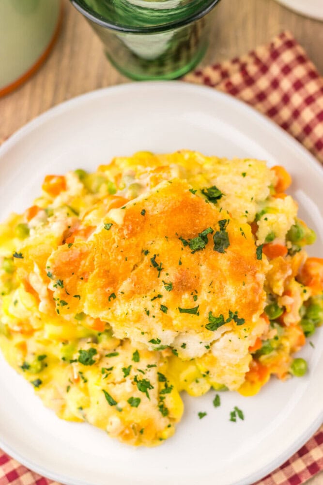Plated chicken cobbler with golden biscuit topping and herb garnish on white plate