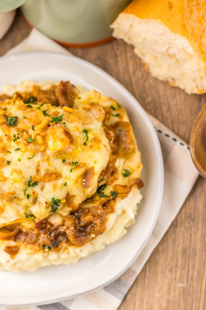French onion chicken bake with caramelized onions and melted cheese, garnished with fresh parsley, served on white plate with crusty bread