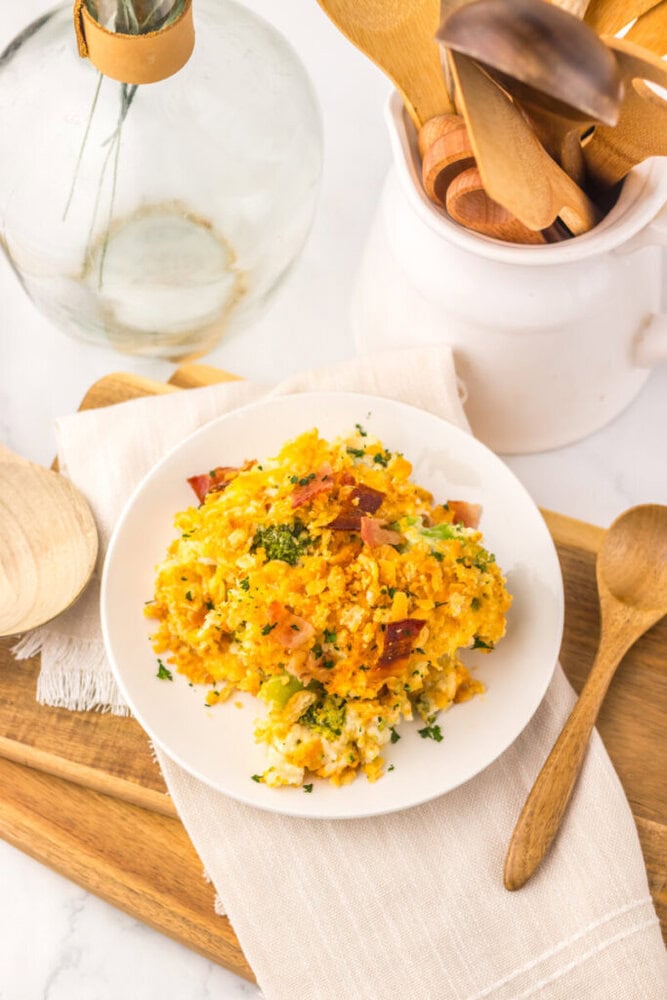 Loaded broccoli rice casserole with corn and bacon garnished with fresh herbs on white plate overhead view
