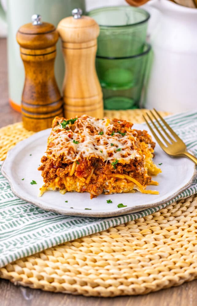 Million Dollar Spaghetti Casserole plated with melted cheese and parsley garnish on white dinnerware