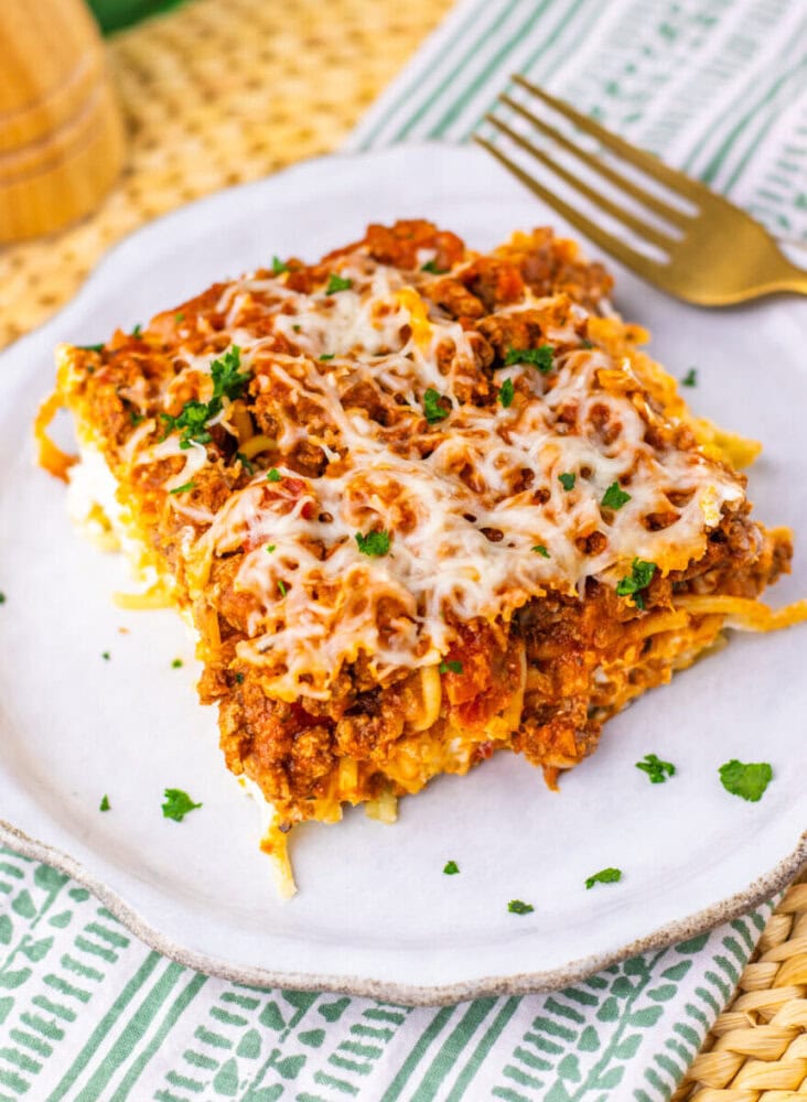 Million Dollar Spaghetti Casserole slice with melted cheese and parsley on white plate