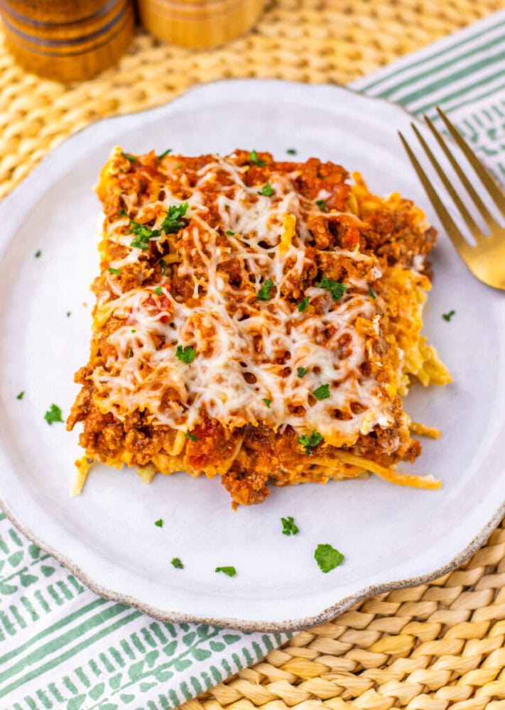 Million Dollar Spaghetti Casserole slice plated with melted cheese and parsley garnish on white dish