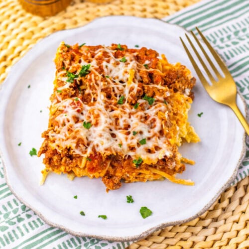 Million Dollar Spaghetti Casserole with melted cheese and parsley garnish on white plate
