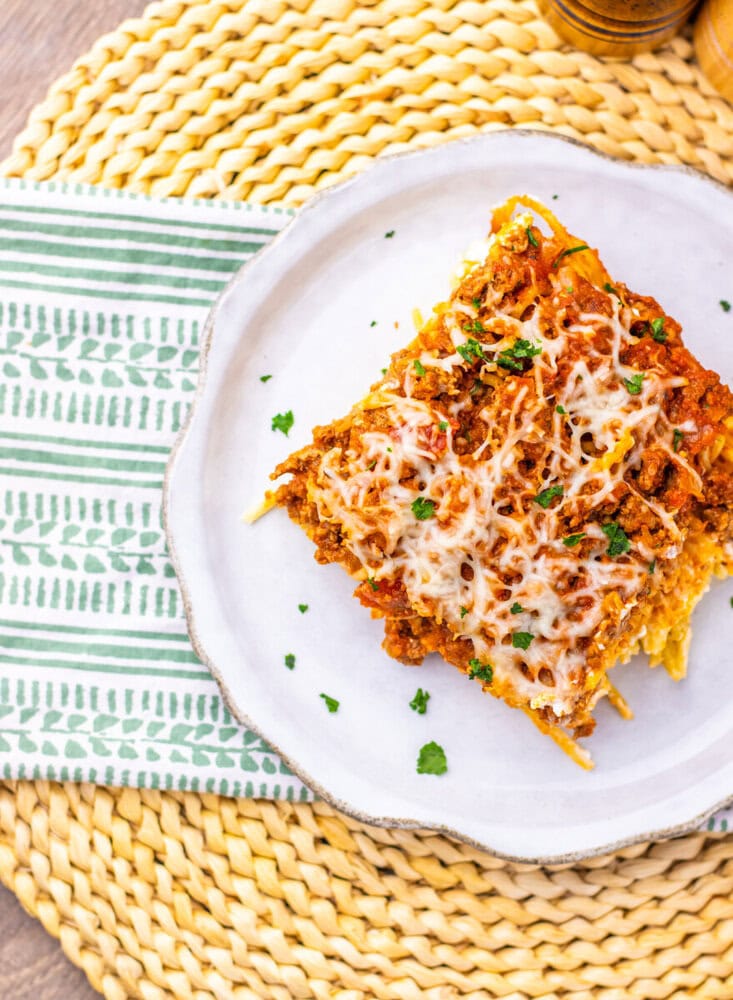 Million Dollar Spaghetti Casserole square with melted cheese and parsley on white plate