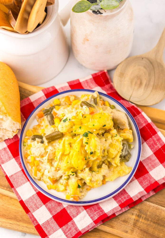 Slow cooker chicken and dumplings pot pie plated in a white bowl with blue rim, topped with fresh herbs, served with bread and beverages
