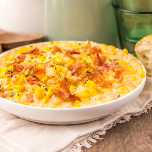 Slow cooker creamy bacon corn chowder in white bowl with corn, bacon, and herbs garnish served with bread