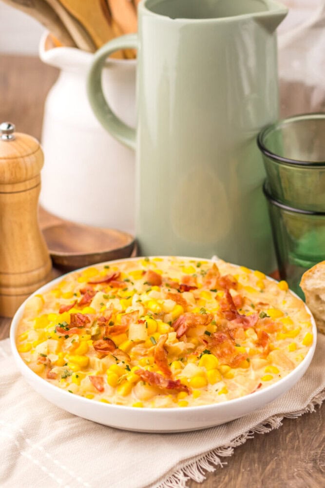 Slow cooker creamy bacon corn chowder served in white bowl with garnish and tableware