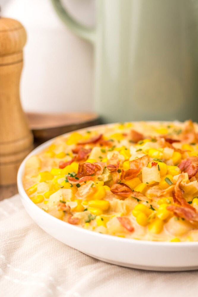 Slow cooker creamy bacon corn chowder in white bowl with corn, potatoes, and bacon garnish