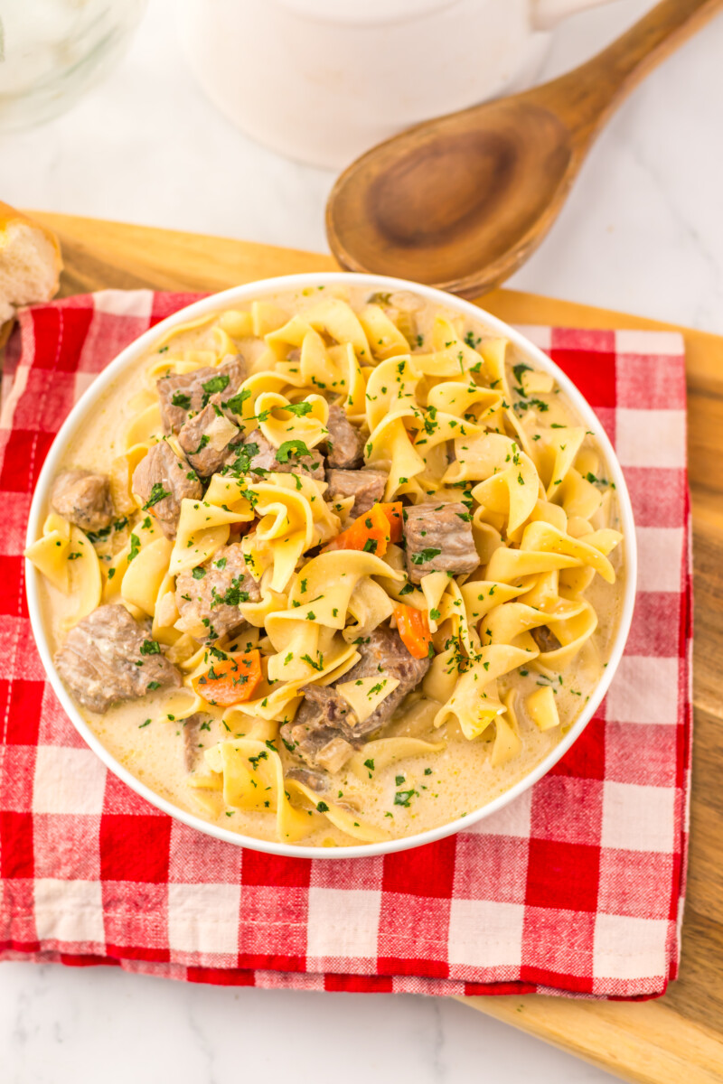 Slow cooker creamy beef noodle soup with tender beef, egg noodles, and fresh parsley garnish in a white bowl