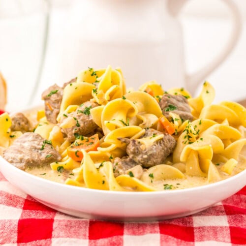 Slow cooker creamy beef noodle soup with shell pasta and herbs in white bowl