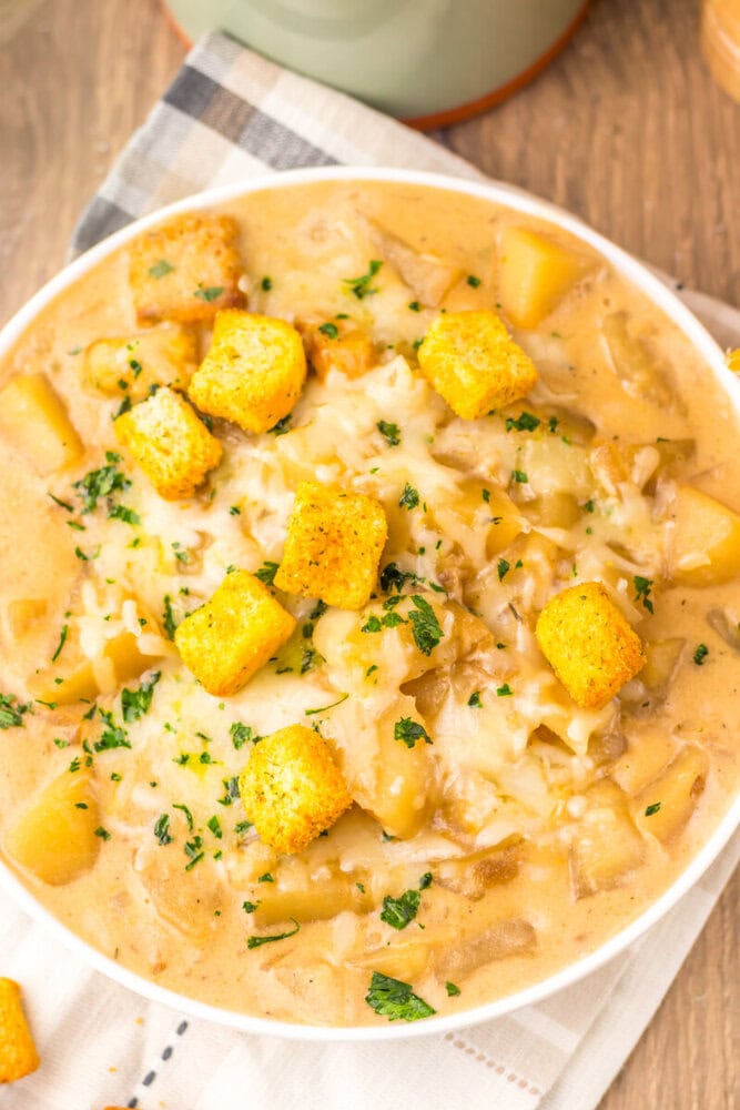 Slow cooker French onion potato soup with golden croutons and parsley garnish in white bowl