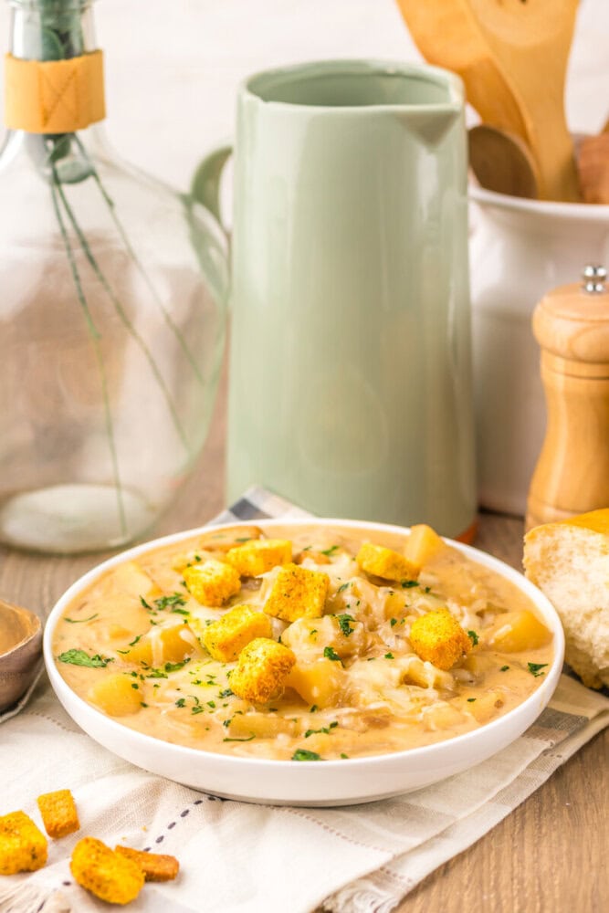 Slow cooker French onion potato soup in white bowl with crispy potato croutons and parsley garnish