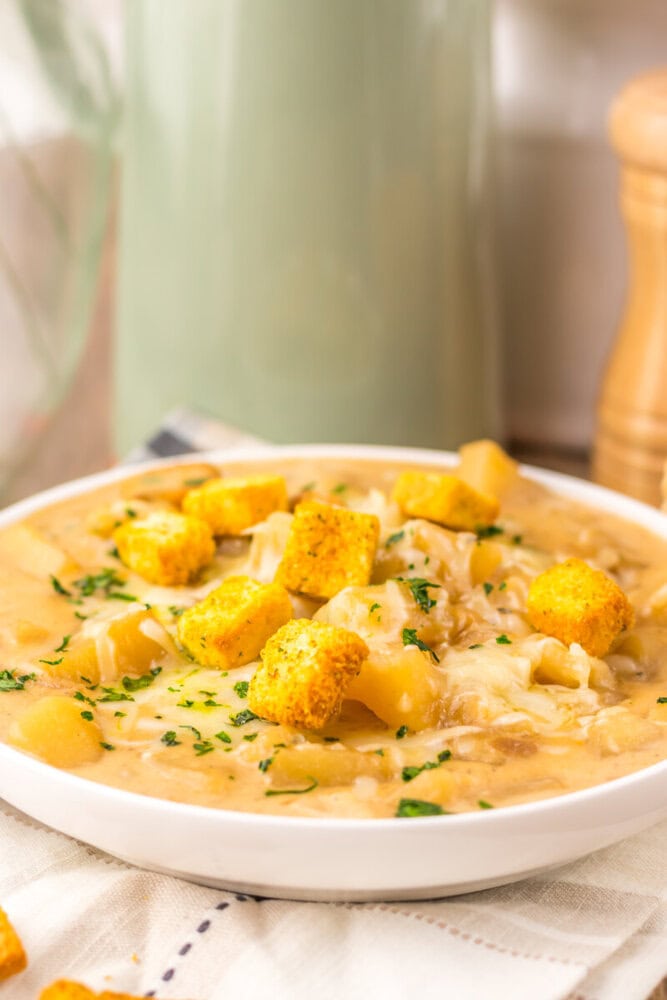 Slow cooker French onion potato soup in white bowl with golden croutons and parsley garnish
