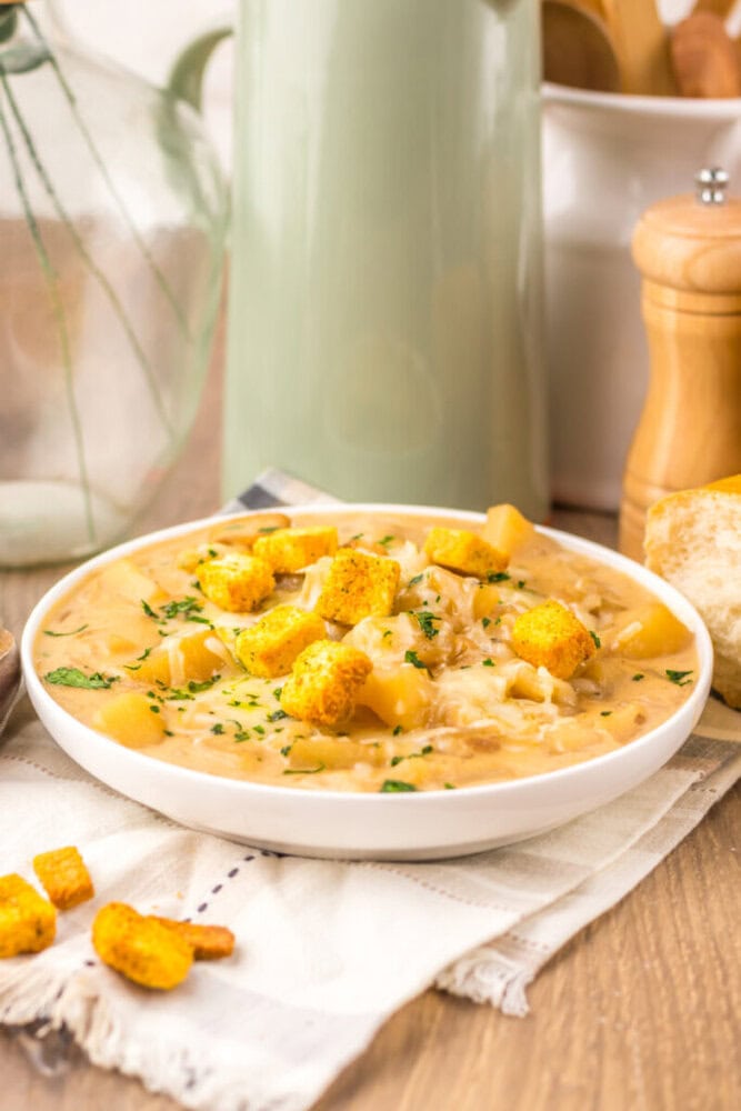 Slow cooker French onion potato soup in white bowl with croutons and chives garnish