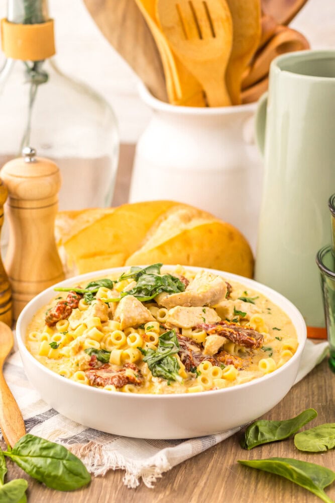 Slow cooker marry me chicken soup with pasta, chicken, and bacon garnished with fresh basil in white bowl