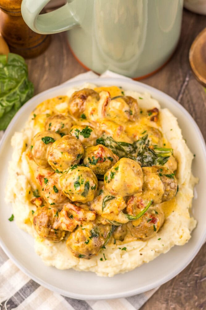 Slow cooker creamy marry me meatballs with herbs served over mashed potatoes on a white plate