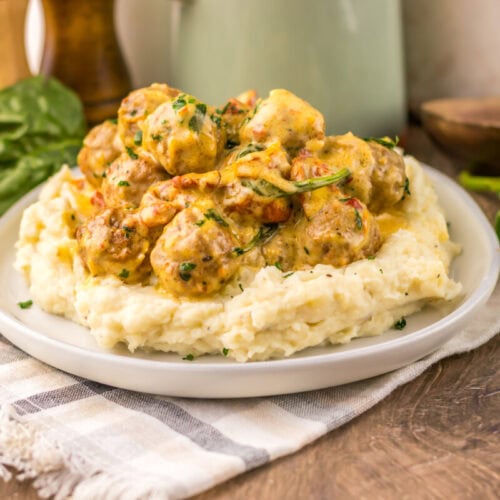 Slow cooker creamy marry me meatballs served over mashed potatoes with fresh basil garnish