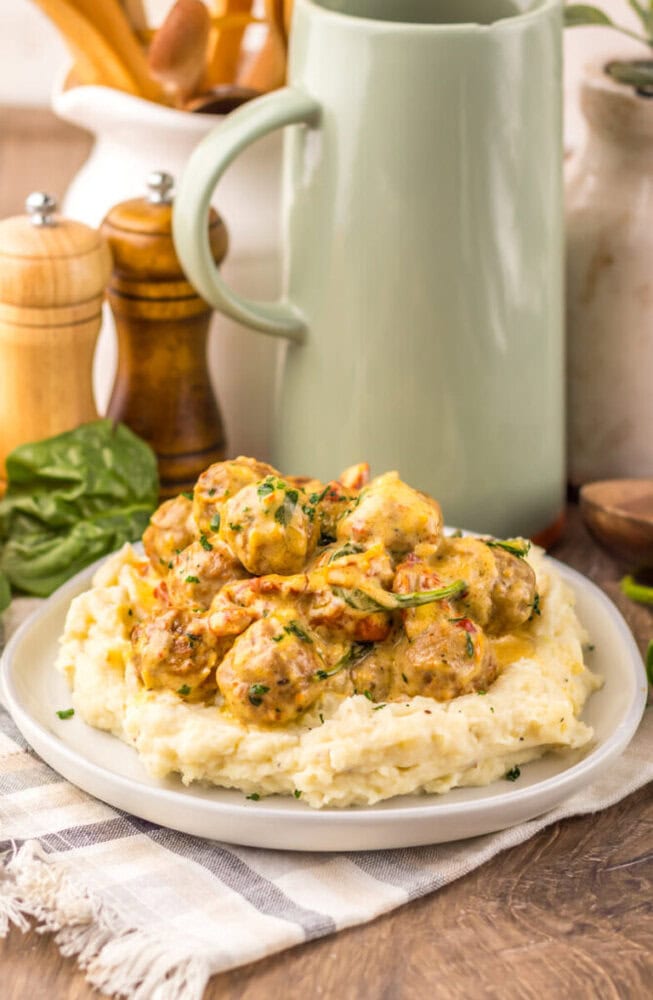 Slow cooker creamy marry me meatballs served over mashed potatoes garnished with chives