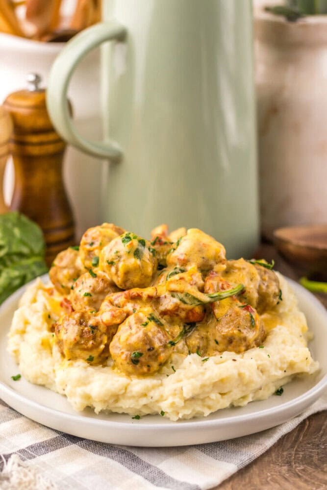 Slow cooker creamy marry me meatballs served over mashed potatoes garnished with chives
